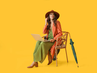 Young fashionable woman sitting in chair with laptop on yellow background