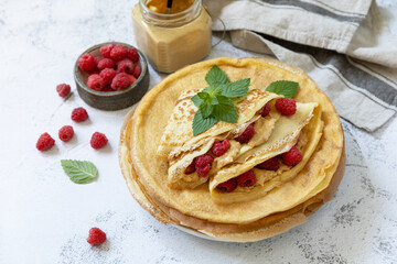 Healthy breakfast, celebrating Pancake day. Delicious homemade crepes with rasberries and peanut paste on a stone tabletop. Copy space.