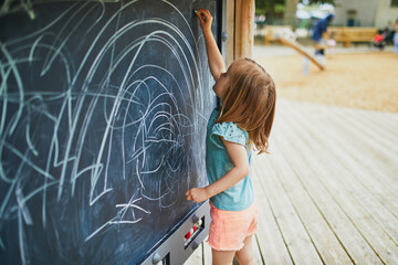 Fototapeta na wymiar Adorable toddler girl drawing with chalks on easel
