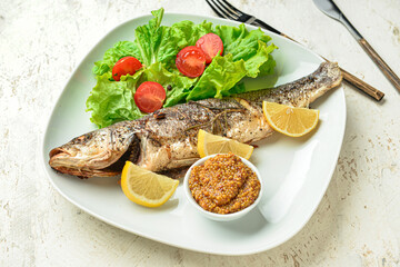 Plate with delicious sea bass fish, vegetables, bowl with mustard seeds and cutlery on light background, closeup