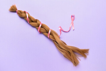 Braided red hair for donation with pink ribbon on lilac background