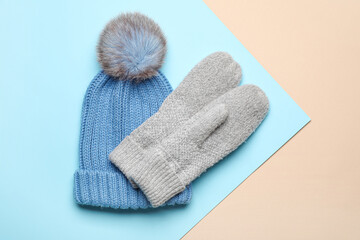 Pair of warm mittens and hat on color background