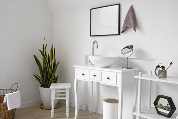 Interior of light bathroom with sink, houseplant and shelving unit
