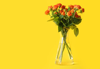 Vase with beautiful orange roses on yellow background