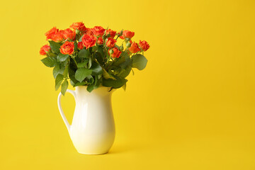 Jug with beautiful orange roses on yellow background