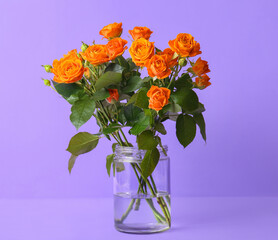 Vase with beautiful orange roses on purple background