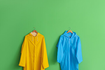 Bright raincoats hanging on green wall