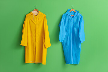 Bright raincoats hanging on green wall