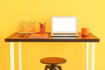 Workplace with modern laptop, stationery supplies and cup near color wall