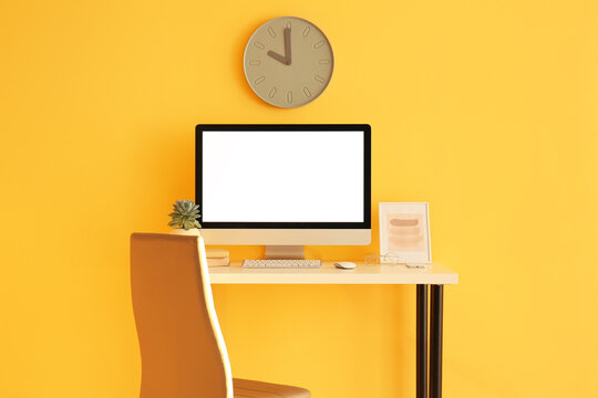 Workplace with modern computer near color wall with clock