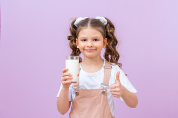 Beautiful child drinks milk for breakfast. A little girl with curly hair holds a glass of cow's milk.