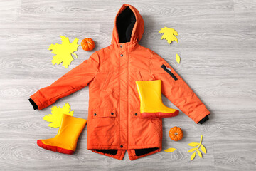 Kid jacket, gumboots and autumn decor on grey wooden background