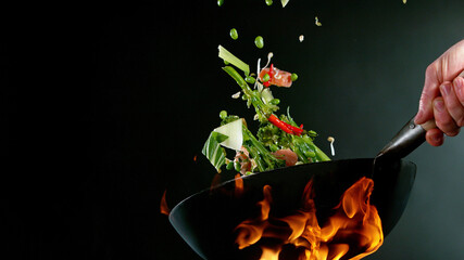 Closeup of chef throwing salmon mix from wok pan in fire. - obrazy, fototapety, plakaty