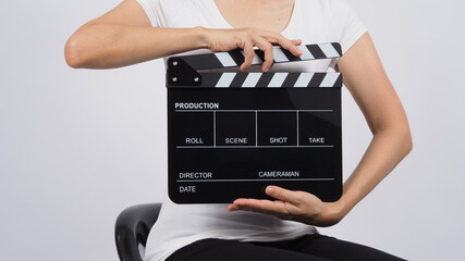 The woman is sitting on the chair and her hands are holding a black Clapperboard or movie slate on white background.