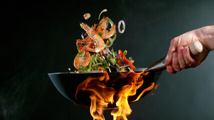 Closeup of chef throwing prawns from wok pan in fire. - 481880392