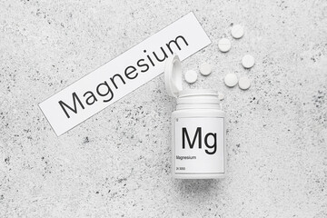 Bottle with pills and word MAGNESIUM on light background
