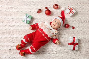 Fototapeta na wymiar Cute little baby in Christmas outfit surrounded by festive items on white knitted plaid, top view. Winter holiday