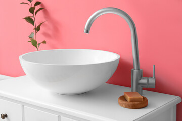 Table with sink, soap and plant branch in vase near pink wall