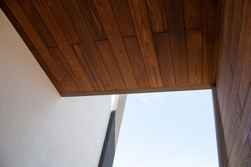 Modern architecture detail of wooden facade cladding, white wall and sky background