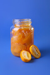Jar of tasty kumquat jam on blue background