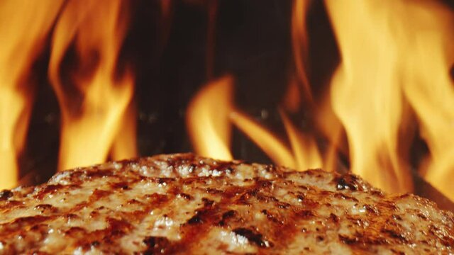 Close up zoom out shot of juicy burger meat being cooked on grill and fire