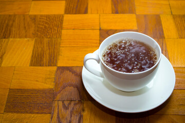 A cup of tea with bubbles stands on a wooden table.