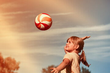 A girl is playing volleyball . The child hits the ball with his hand . Outdoor play