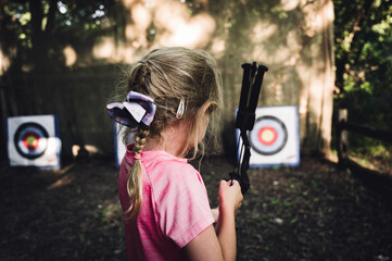 Young girl at summer camp learning to use a bow and arrow looking down field at the target.