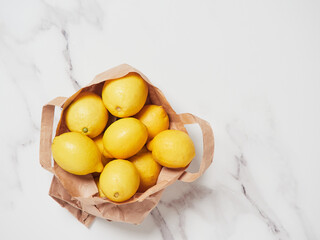 many yellow lemons in a paper bag isolated on a marble countertop as background, top view with copy...