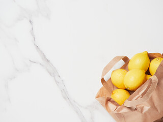 paper bag full of yellow lemons on marble countertop background, placed in the lower right corner, top view with copy space