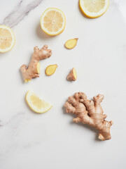 lemon slices and pieces of fresh, whole and sliced ginger root spread on marble countertop, top view
