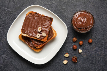 Plate of bread with chocolate paste and hazelnuts on black background