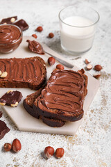 Bread with chocolate paste, hazelnuts and glass of milk on light background