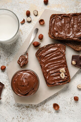 Bread with chocolate paste, hazelnuts and glass of milk on light background