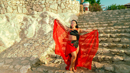 A woman in a red costume dances an oriental dance on a stone staircase.