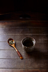 Green tea (sencha) in a traditional, japanese tea cup and sencha leaves on a wooden tea spoon. Dark wooden background.	