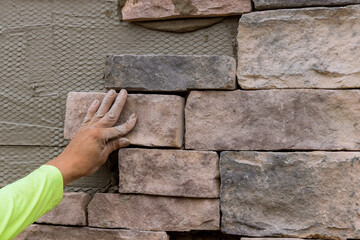 The process of worker laying decorative bricks stone on the wall.