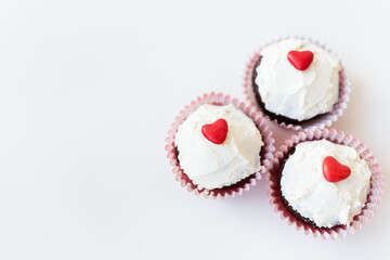 Valentine-14 February. Sweet chocolate muffins with butter cream and a red heart for decoration on a white background.