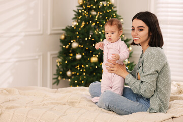 Happy young mother with her cute baby on bed at home, space for text. Winter holiday