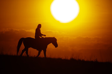 silhouette of a woman riding a horse with the big sun overhead