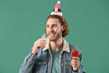 Handsome man with gingerbread cookie drinking milk on green background