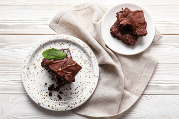 Plates with pieces of tasty chocolate brownie on white wooden background