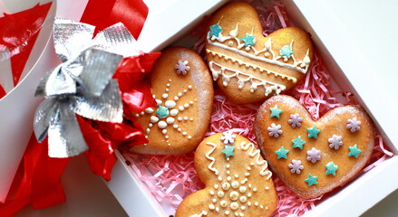 Four homemade gingerbread in shape heart paper box, white icing patterns, decorated with green purple star flower lie on pink paper confetti white background, view from above. Gift for valentine's day