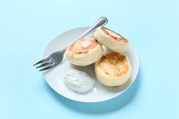 Plate with tasty cottage cheese pancakes and sauce on blue background