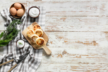 Board with tasty cottage cheese pancakes, sauce and eggs on light wooden background