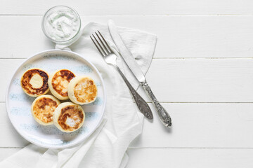 Plate with tasty cottage cheese pancakes and sauce on light wooden background