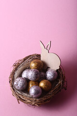 Easter concept - rabbit in a nest with chocolate eggs against pink background