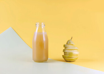 bottle of pear juice with pulp and fresh pear cut in layers on a yellow background