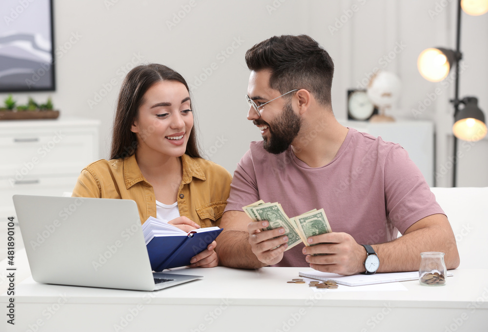 Wall mural Happy young couple counting money at white table indoors