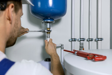 plumber installing expansion tank for house heating system. plumbing service - obrazy, fototapety, plakaty
